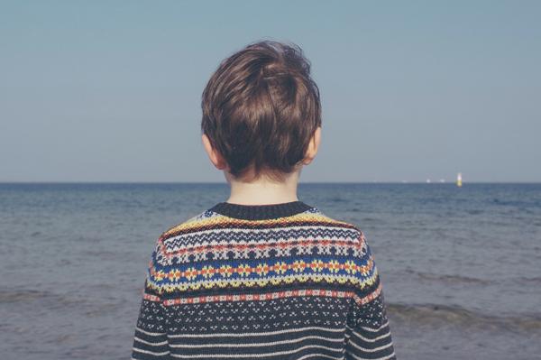 boy wearing multicolored striped floral sweater facing the sea